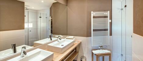 A modern bathroom with two sinks, a mirror, a towel rack, and a shower area.