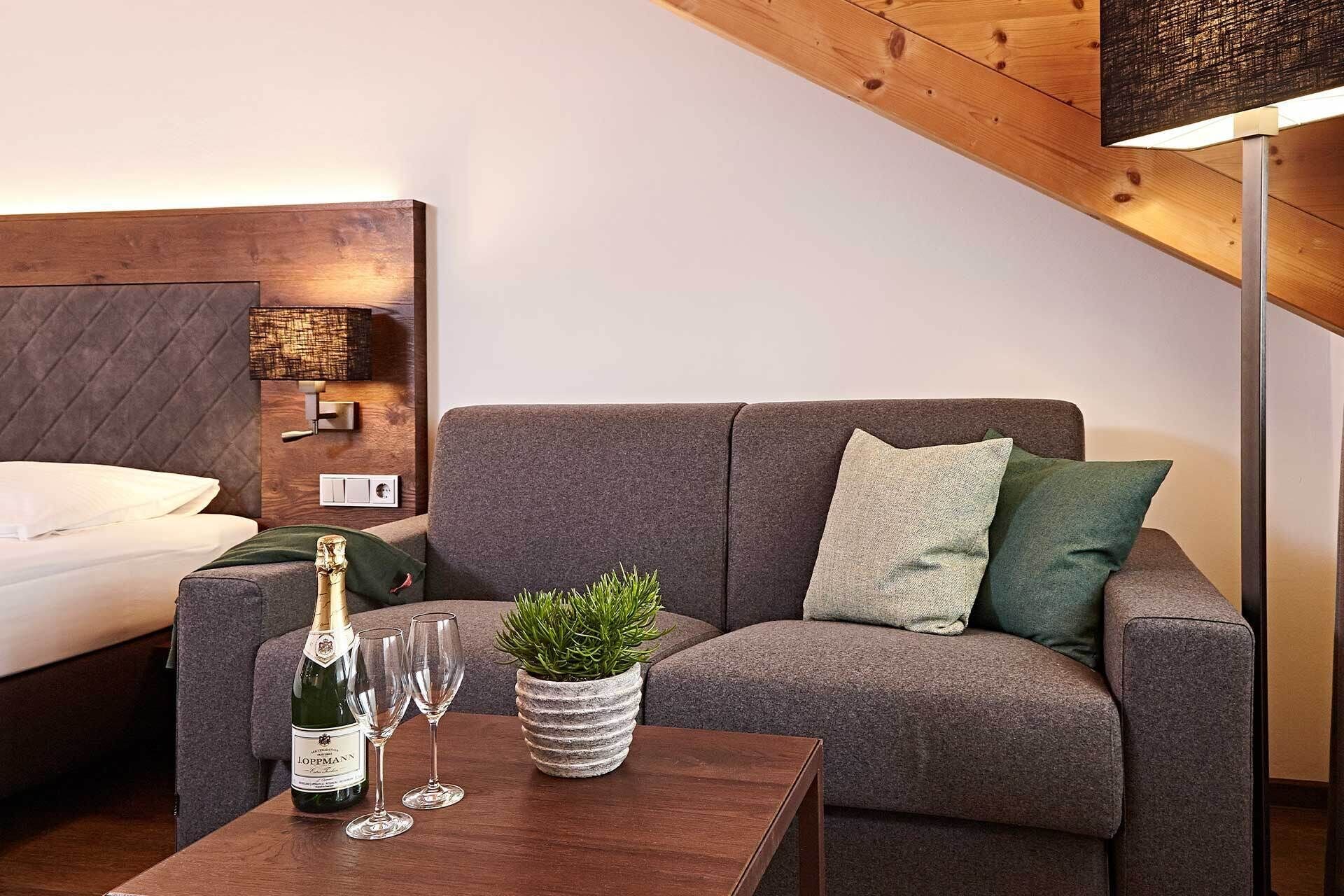 Ein modernes Wohnzimmer mit einem grauen Sofa, einem Holztisch, einer Champagnerflasche, zwei Gläsern und einer kleinen Topfpflanze.
