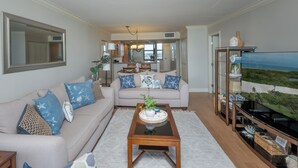 Ein Wohnzimmer mit einem beigefarbenen Sofa, blauen Kissen mit Muster, einem Holztisch und Blick auf die Küche und den Essbereich.