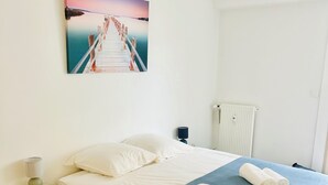 Un dormitorio con cama, una mesita de noche con lámpara, un cuadro en la pared y un radiador.