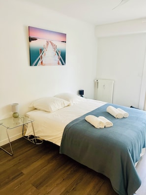 A bedroom with a bed, a bedside table with a lamp, a picture on the wall, and a radiator. - Very nice apartment in carré d'or - 3* - City center and beaches (Antibes)