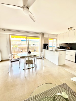 A modern kitchen with a central island, a dining area with clear chairs, and a view of a balcony with yellow awnings. - Very nice apartment in carré d'or - 3* - City center and beaches (Antibes)