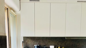 Una cocina moderna con un lavamanos negro, grifo de acero inoxidable y armarios blancos. Hay una encimera con un hervidor, tostadora y frascos amarillos.