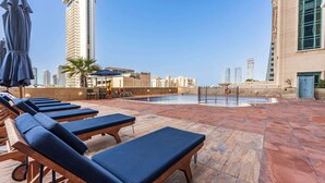 A rooftop pool area with lounge chairs and umbrellas, surrounded by high-rise buildings. - StayShort - Cozy Dubai Marina Stay with Private Balcony Sleeps 2 (Dubai Marina)