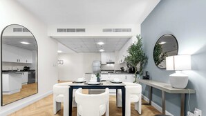 A modern kitchen with white cabinets, a dining area with a dark table and white chairs, and a large mirror on the wall. - StayShort - Cozy Dubai Marina Stay with Private Balcony Sleeps 2 (Dubai Marina)