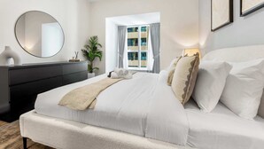 A bedroom with a bed, a dresser, a mirror, a window with curtains, and a plant. - StayShort - Cozy Dubai Marina Stay with Private Balcony Sleeps 2 (Dubai Marina)