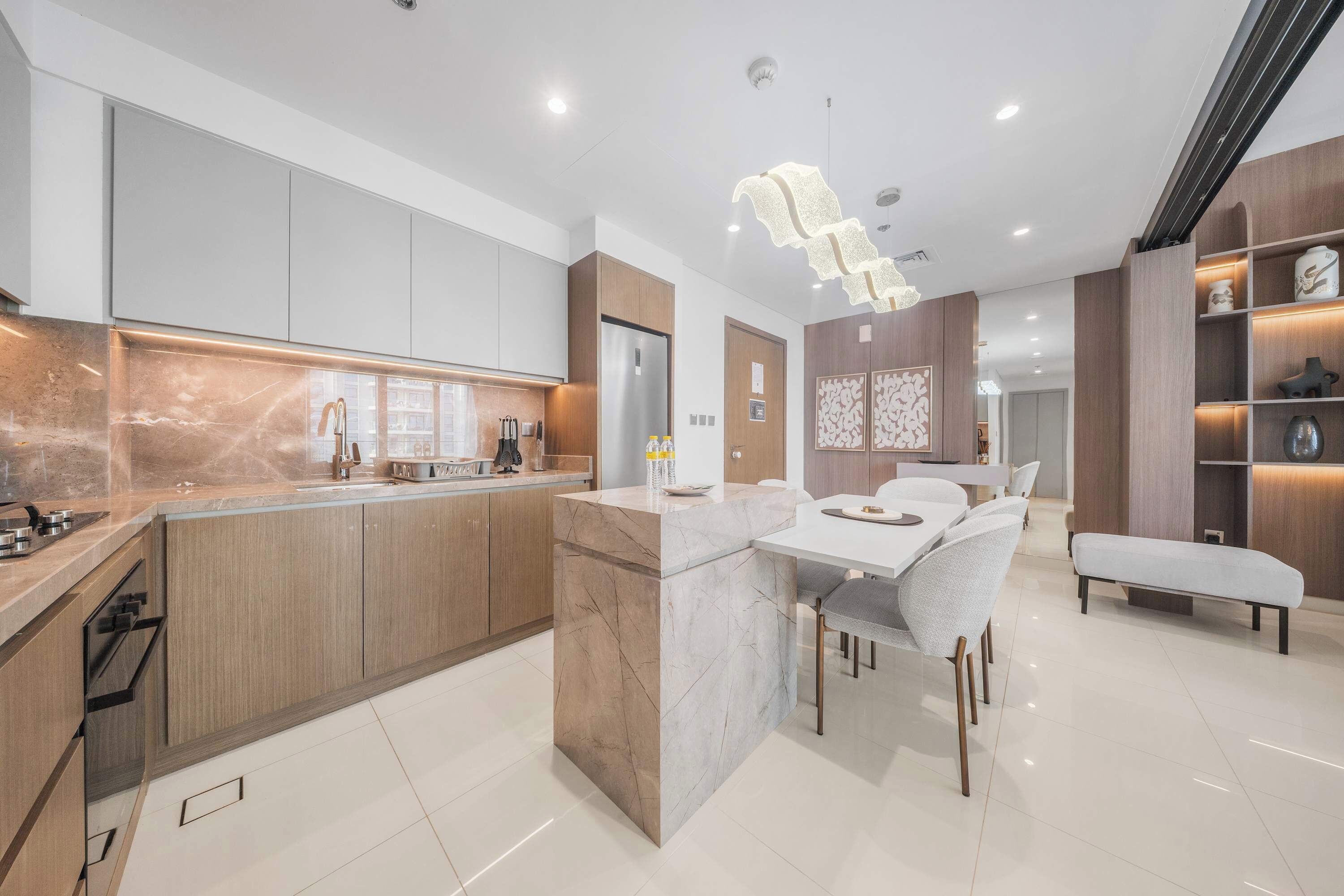 A modern kitchen with a marble island, wooden cabinets, and a dining area with a bench.