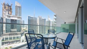 Un balcon doté d’une rambarde en verre, d’une table ronde et de deux chaises bleues.