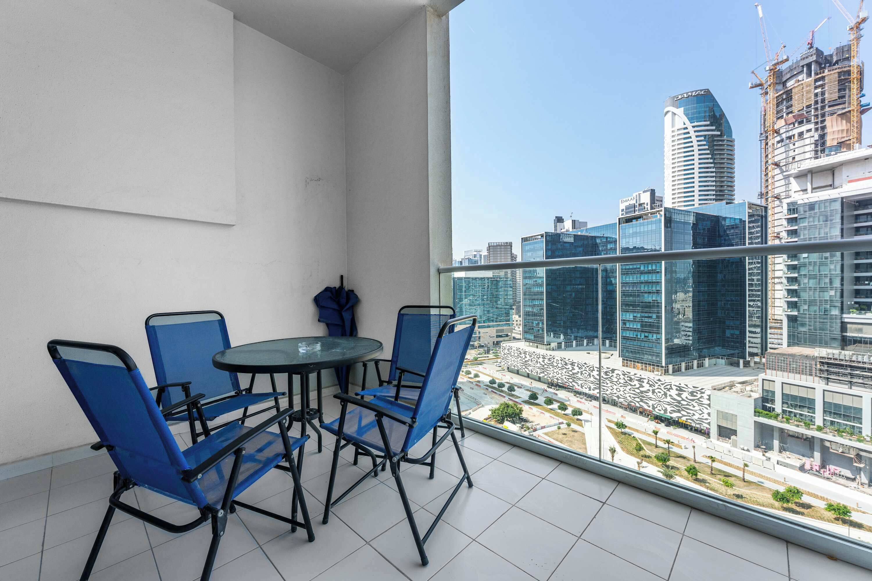 Ein Balkon mit Tisch und Stühlen, Blick auf eine Stadtlandschaft mit modernen Gebäuden und Baukränen.