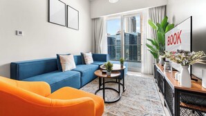 Un salon moderne avec un canapé bleu, un fauteuil orange, une petite table basse et une bibliothèque sur laquelle on peut lire l’inscription « LIVRES ».