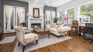 A living room with a fireplace, two sofas, a coffee table, and a chandelier. - Walkable Hillsboro Home - Near 12 South & Vandy (Nashville)