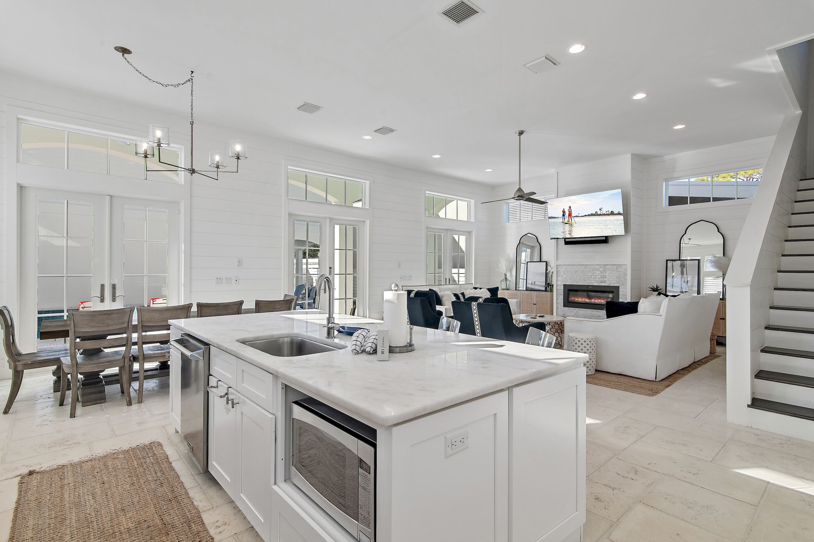 A spacious kitchen with a central island, a dining area with wooden chairs, and a living area with a sofa and fireplace.