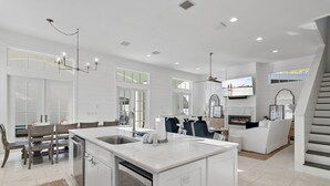 A spacious kitchen with a central island, a dining area with wooden chairs, and a living area with a sofa and fireplace. - Stunning New Main & Carriage House w/ Private Pool- Seas the Day of Seagrove (Santa Rosa Beach)