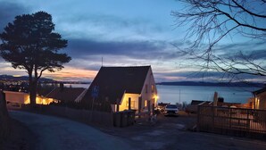 A house with a sloped roof, a bicycle path sign, and a view of a body of water at dusk.