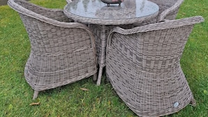 A round wicker table with four chairs, a glass top, and a flower centerpiece.