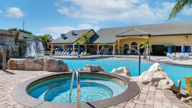 A pool area with a hot tub, lounge chairs, and a waterfall feature. - Family Resort Getaway w Pool Patio Near Disney (Kissimmee)