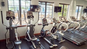 A gym with various cardio machines, large windows, and a TV mounted on the wall. - Family Resort Getaway w Pool Patio Near Disney (Kissimmee)