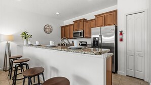 A modern kitchen with wooden cabinets, stainless steel appliances, a marble countertop, and bar stools. - Family Resort Getaway w Pool Patio Near Disney (Kissimmee)