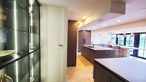 Eine moderne Küche mit einer zentralen Kochinsel, Edelstahlgeräten und Blick ins Freie durch große Fenster.