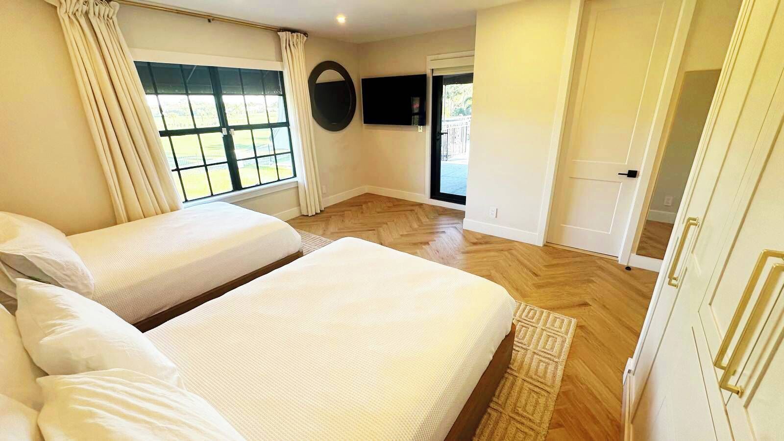 Un dormitorio con dos camas, un ventanal grande, un televisor de pantalla plana y una puerta que da a un balcón.