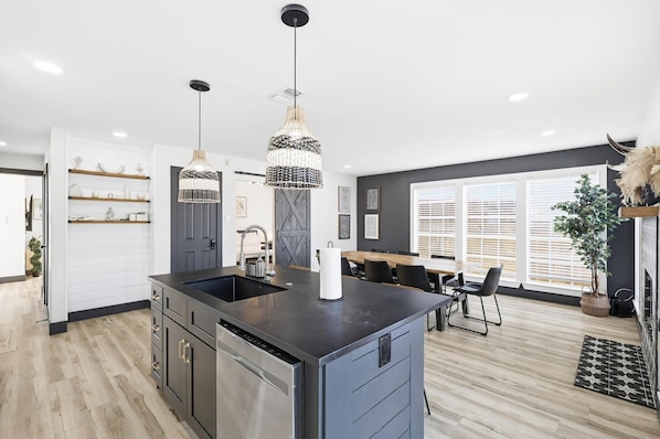 A modern kitchen with a central island, pendant lights, and a dining area with a table and chairs.