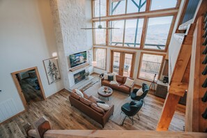 A spacious living area with a fireplace, large windows, and a high ceiling.