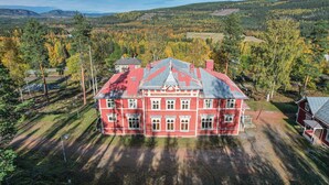A large red building with a symmetrical facade and multiple windows, surrounded by a forested landscape. - Porter House Tingshus (Hammarstrand)