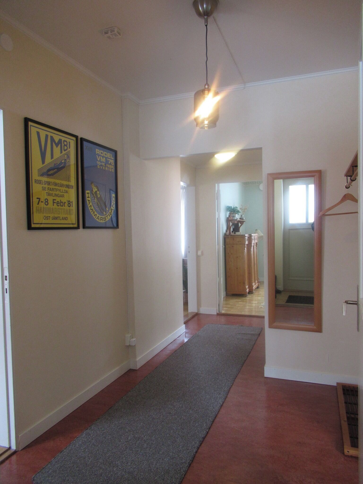 A hallway with a grey carpet, white walls, and two framed posters on the left.