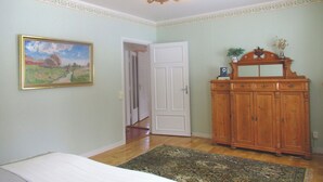 A bedroom with a bed, a wooden dresser, a painting, and a door leading to another room. - Porter House Tingshus (Hammarstrand)