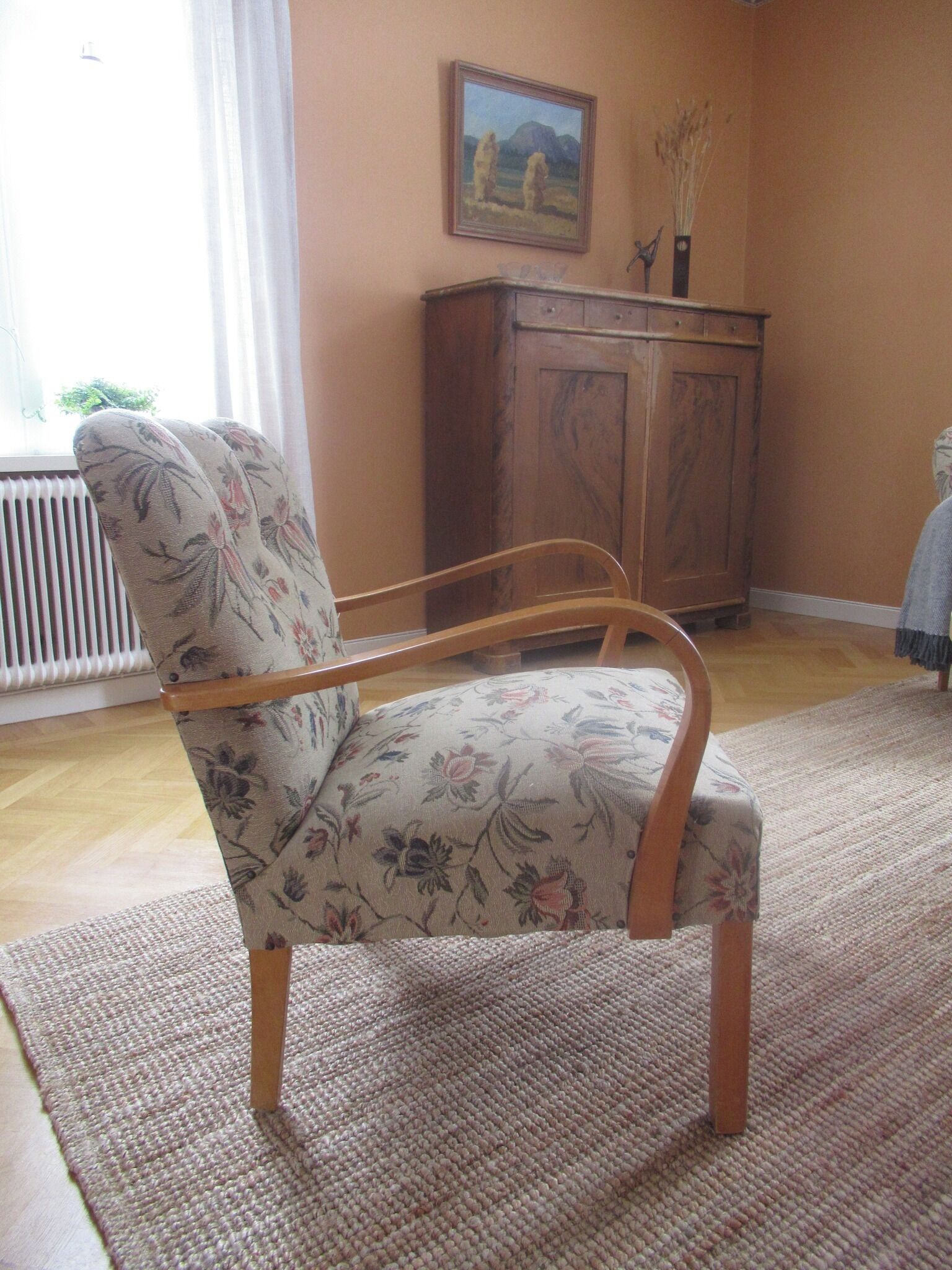 Un soggiorno con una poltrona floreale, un mobiletto in legno e un quadro appeso al muro.