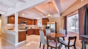 A modern kitchen with wooden cabinets, a central island, and a dining area with patterned chairs. - Iroquois Ridge Charming Home for 8 w/ Hot Tub Near Lake Tahoe & Skiing (South Lake Tahoe)