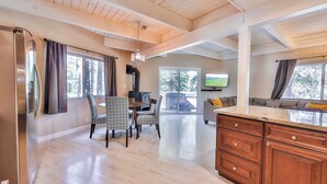 A spacious kitchen with wooden cabinets, a dining area with patterned chairs, and large windows offering a view of the outdoors. - Iroquois Ridge Charming Home for 8 w/ Hot Tub Near Lake Tahoe & Skiing (South Lake Tahoe)