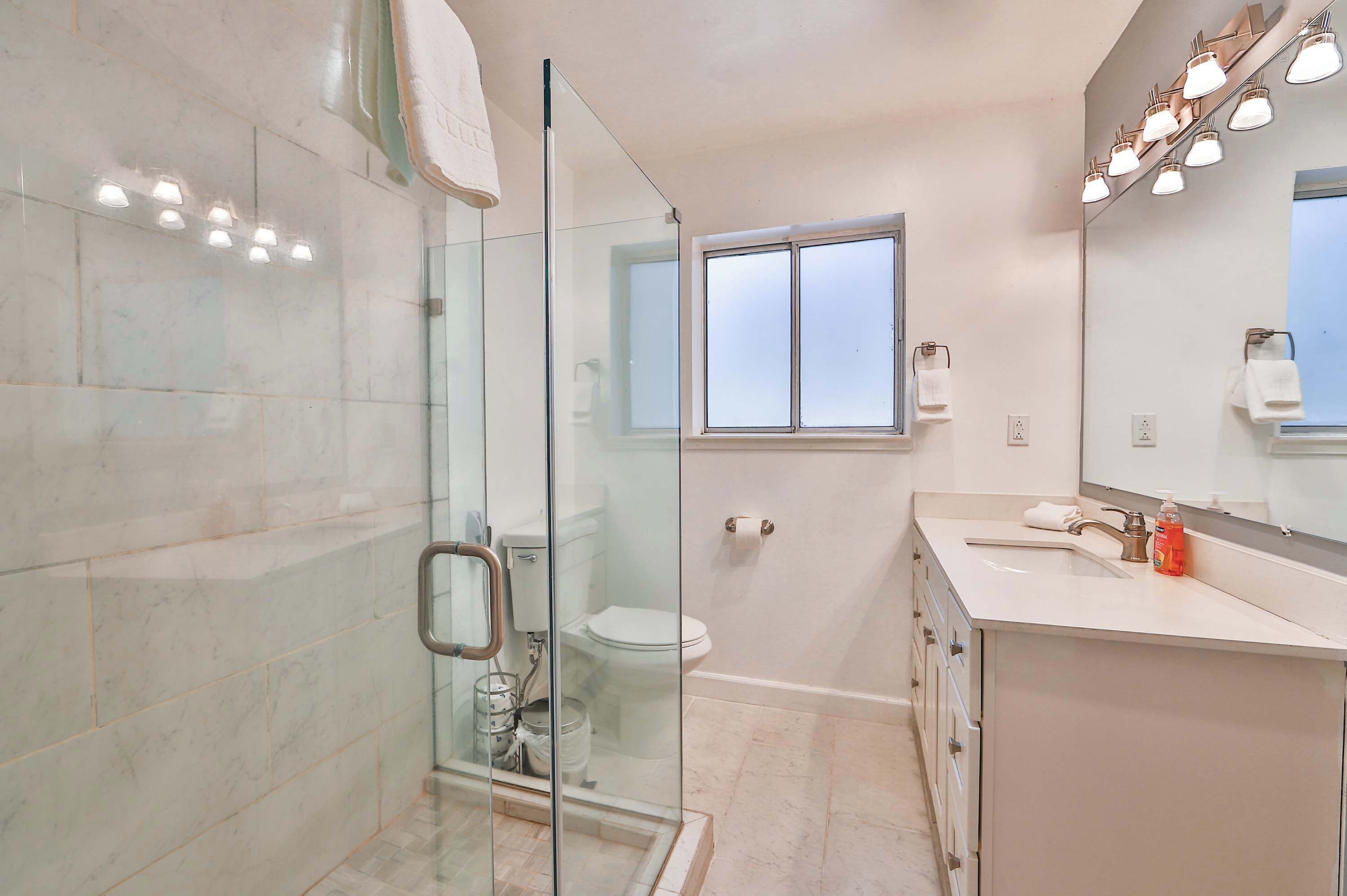 A modern bathroom with a glass shower enclosure, a toilet, and a sink with a mirror above.