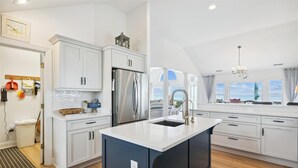 A modern kitchen with white cabinetry, a stainless steel refrigerator, and a large island with a sink. - SS3 - Oceanfront 6 bedroom, 5 bath, dune top deck w/ hot tub, billiards table (Southern Shores)
