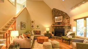 Una sala de estar con chimenea de piedra, una escalera y un conjunto de sofás.