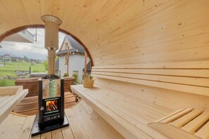 Un sauna avec un intérieur en bois, un banc et une vue sur une maison, visible à travers une ouverture en arc de cercle.