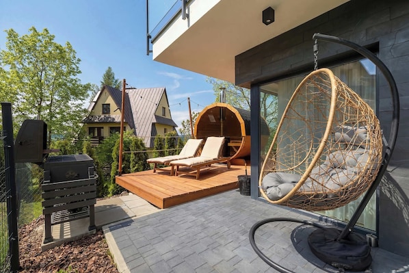 Eine moderne Terrasse im Freien mit Grill, Liegestühlen und einer Hängematte.