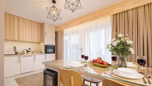 A modern kitchen with wooden cabinets, a glass dining table, and a built-in oven. - Spacious Apartment in Zakopane | Terrace with a View, Sauna, Parking (Zakopane)