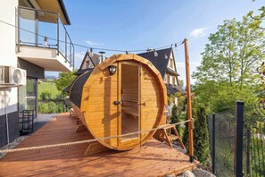 Une structure en bois en forme de tonneau, dotĂ©e dâune porte, dâune terrasse en bois et dâune clĂŽture en mĂ©tal.