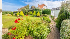 A well-maintained garden with neatly trimmed hedges, a brick pathway, and a house with a red roof in the background. - Greentiles, Sheringham, Norfolk (Sheringham)