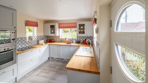 A modern kitchen with white cabinets, a wooden countertop, and a large window with a view of greenery. - Greentiles, Sheringham, Norfolk (Sheringham)