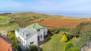 A white house with a green roof, surrounded by a well-maintained lawn and hedges, overlooking a coastal landscape. - Greentiles, Sheringham, Norfolk (Sheringham)