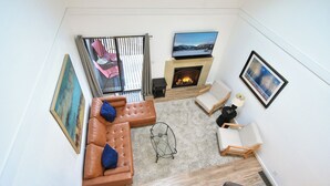 Een moderne woonkamer met een open haard, een bank, een fauteuil en uitzicht op de natuur.