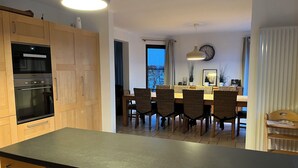 A modern kitchen with wooden cabinets, a built-in oven, and a dining area with wicker chairs and a wooden table. - Les Scailletons, furnished vacation home for 9 people in Neufchâteau Belgian Ardennes (Neufchâteau)