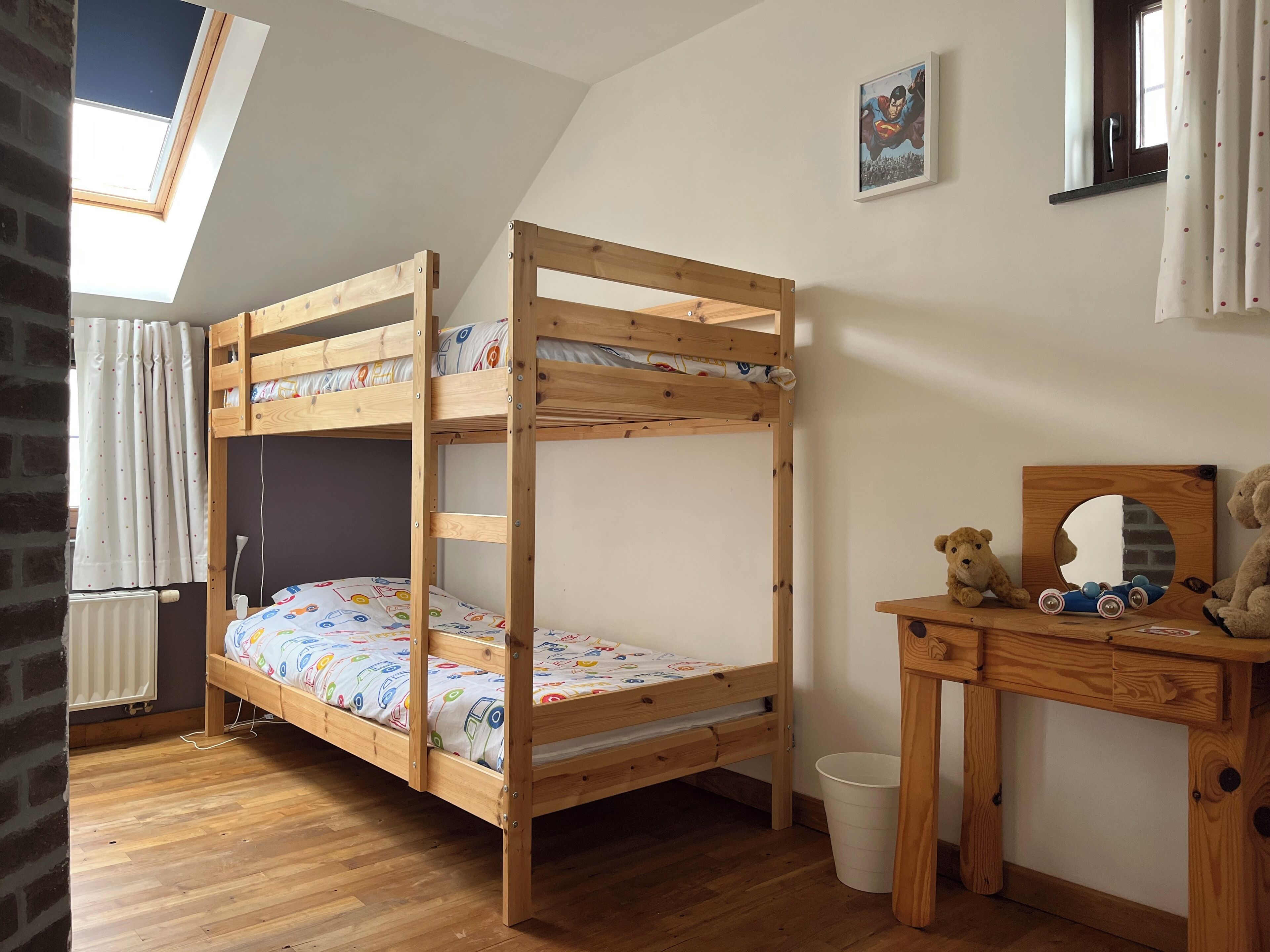 Un lit superposé avec une structure en bois, un bureau avec un miroir et un ours en peluche.