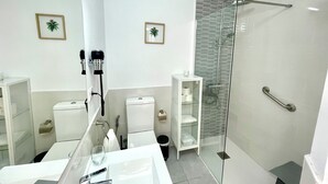 A modern bathroom with a glass-enclosed shower, a white sink, and two framed plants on the wall.