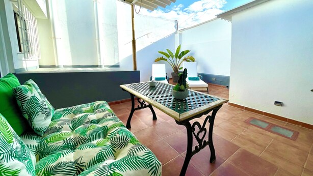 A balcony with a sofa, a table, and potted plants.