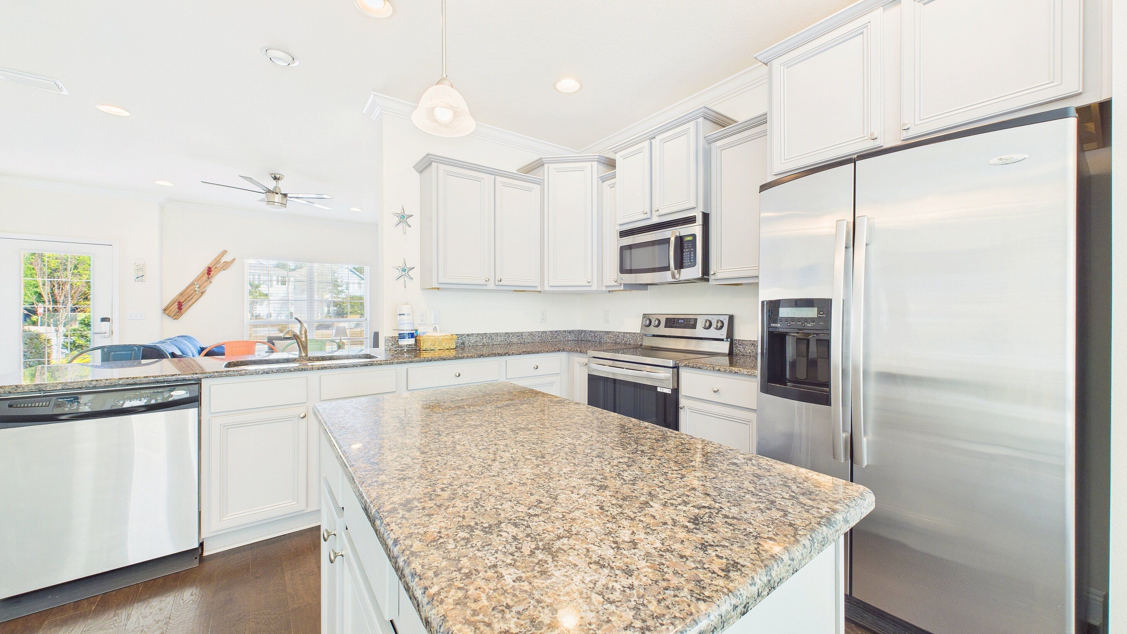 A modern kitchen with white cabinetry, stainless steel appliances, granite countertops, and a large island.
