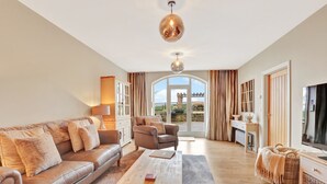 A spacious living room with a sofa set, a coffee table, and a TV. There is a large window with curtains, a fireplace, and a view of the outdoors. - The Retreat at Glenridge House - North East Escapes (Wooler)