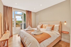 A spacious bedroom with a large bed, a wooden bench, and a view of the outdoors through a glass door.